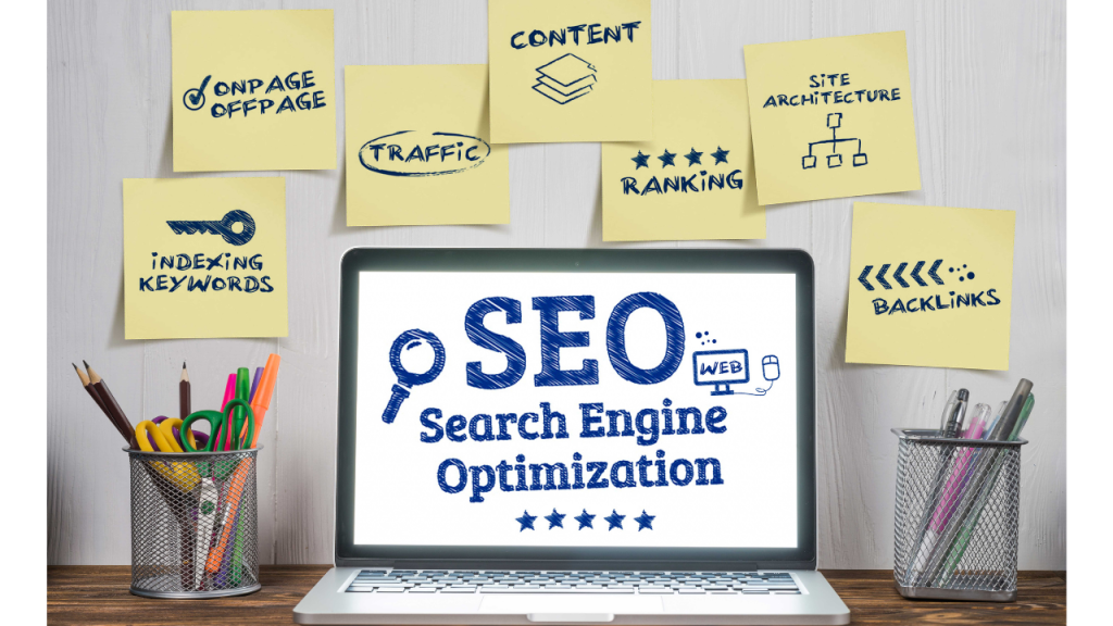 パソコンの画面にSEO（Search Engine Optimization）の表示と、壁にはいくつかの付箋紙が貼られている。